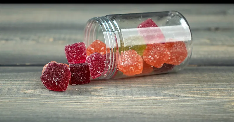 Colorful sugar-coated CBD gummies spilling from a jar